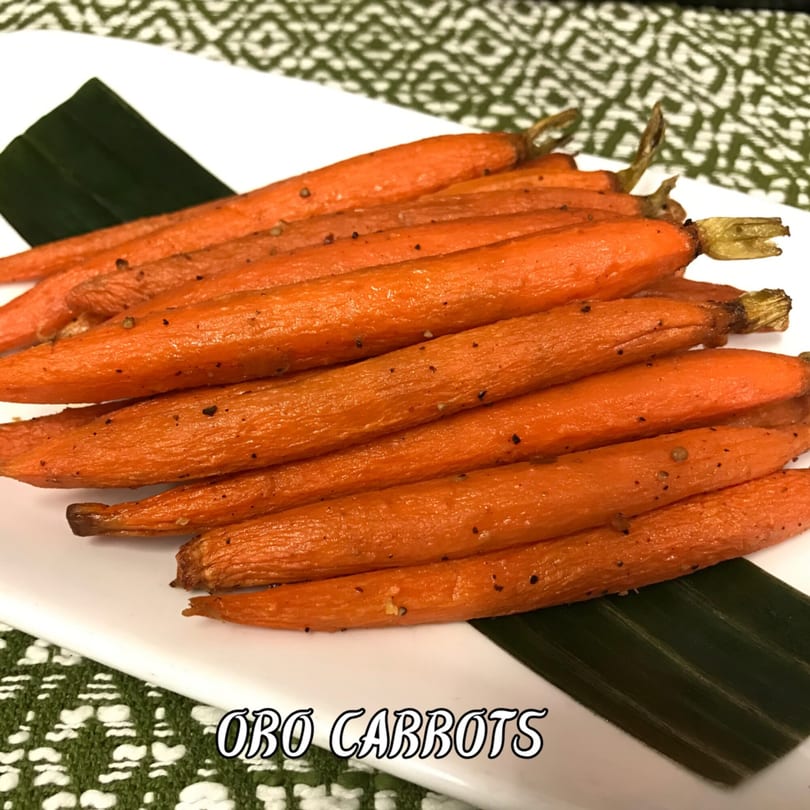 Roasted carrots seasoned with pepper, served on a white plate with a green leaf garnish.