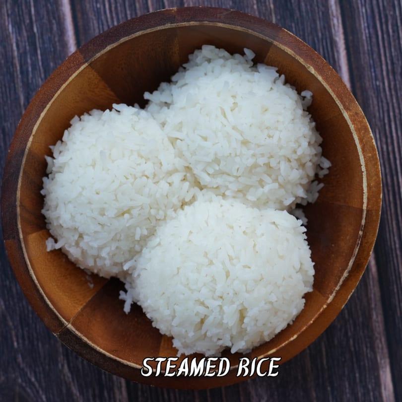 Three mounds of white steamed rice in a wooden bowl on a dark wooden table.