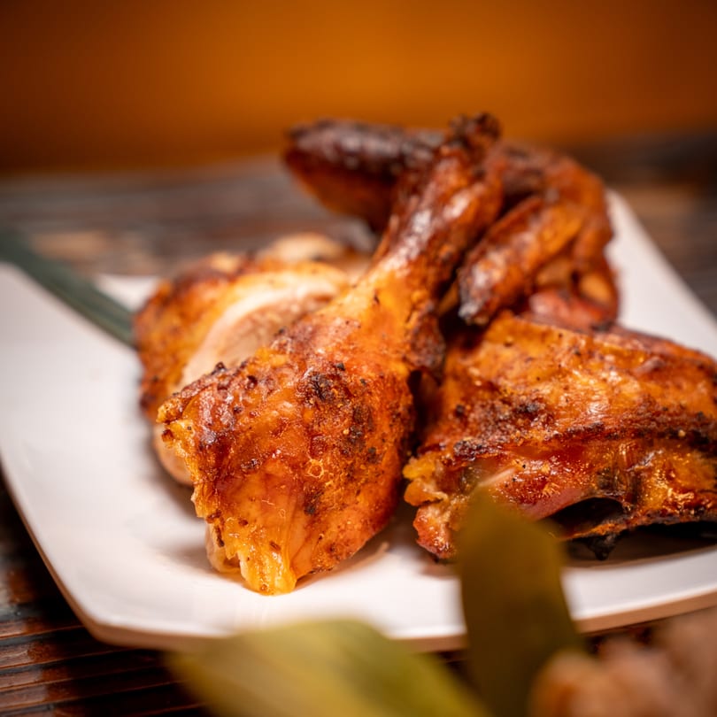 Close-up of golden-brown grilled chicken pieces on a white plate, showcasing crispy skin and juicy meat.