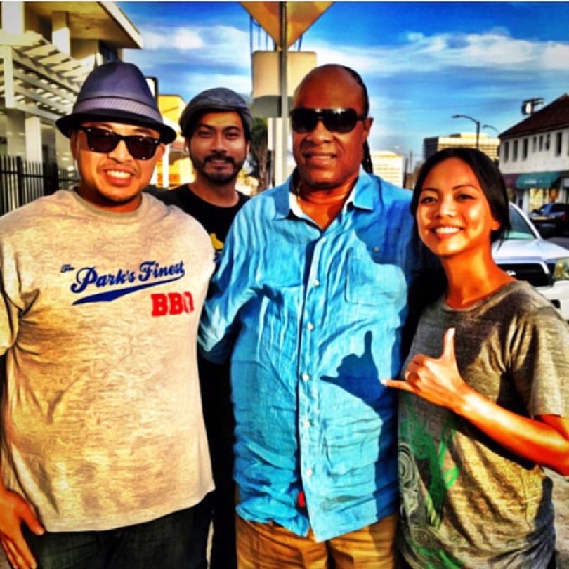 Four smiling people, including one in a "The Park's Finest BBQ" shirt, stand outdoors.