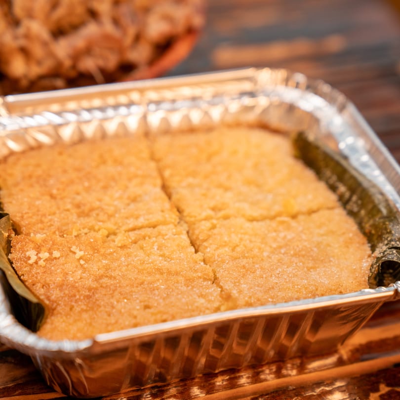 Filipino bibingka, a baked rice cake, in a foil pan, topped with sugar and cut into squares.