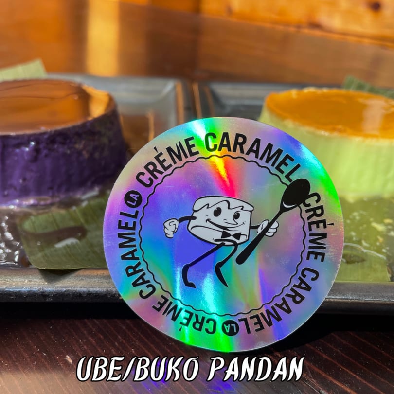 Holographic Crème Caramel logo sticker with two flans, ube and buko pandan, in the background.