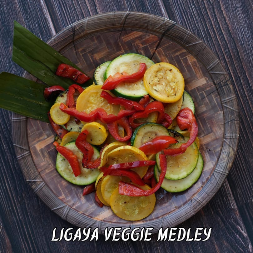 Ligaya Veggie Medley with grilled zucchini, yellow squash, and red bell peppers on a woven plate.