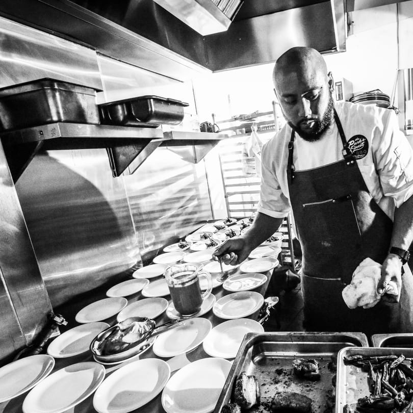 Black and white of a chef plating Filipino dishes in a busy kitchen at The Park's Finest.