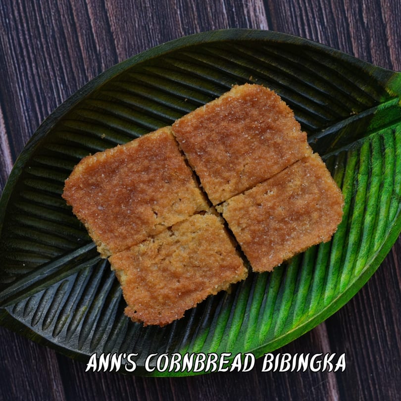 Four square pieces of Ann's Cornbread Bibingka, sprinkled with sugar, on a green leaf-shaped plate.